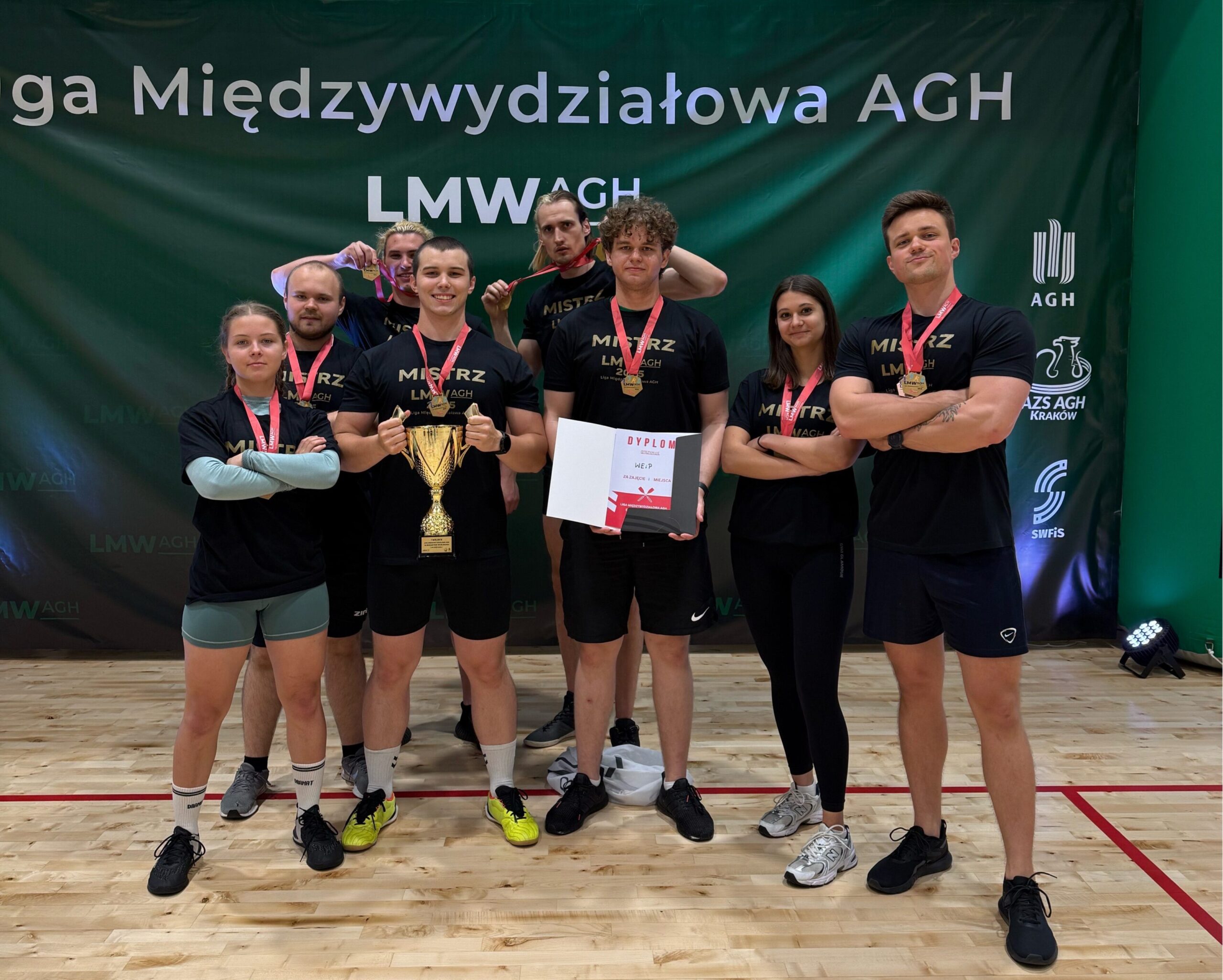 Zwycięska drużyna pozuje z pucharem i medalami na tle baneru Ligi Międzywydziałowej AGH